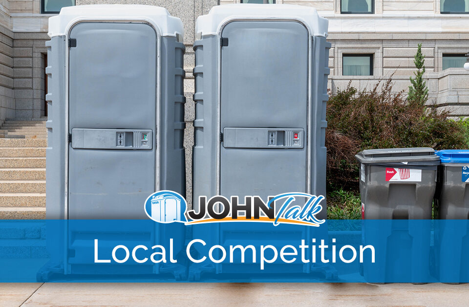 Two portable restrooms and two garbage cans in front of a building