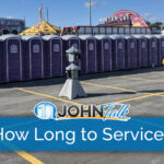 A row of purple portable toilets, along with two hand sanitizer stands and a portable sink at a carnival