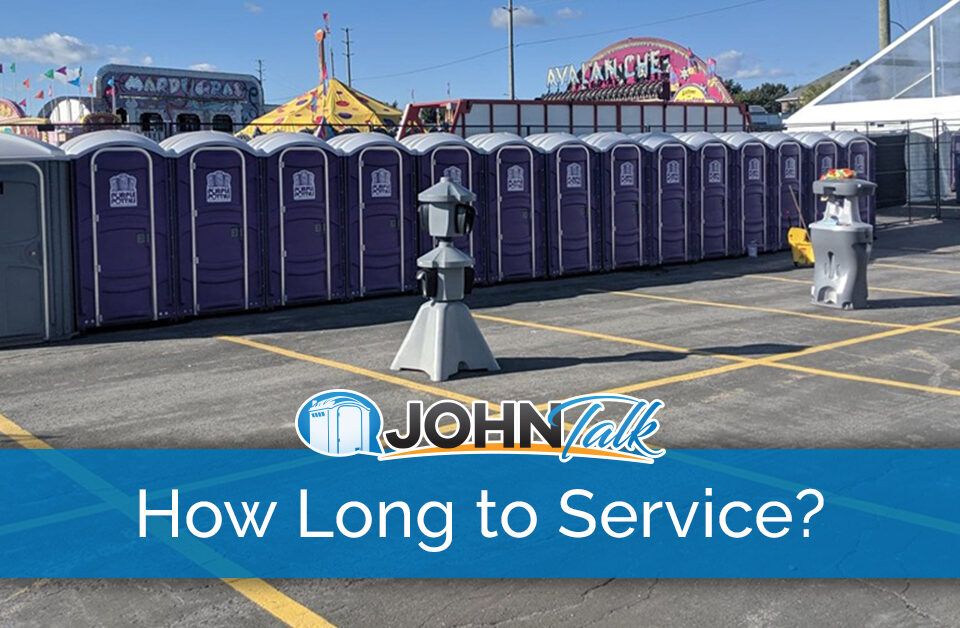 A row of purple portable toilets, along with two hand sanitizer stands and a portable sink at a carnival