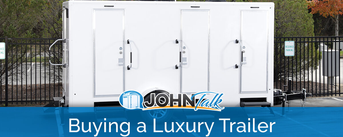 A white luxury restroom trailer in a parking lot with a fence and trees in the background