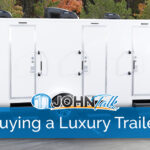 A white luxury restroom trailer in a parking lot with a fence and trees in the background