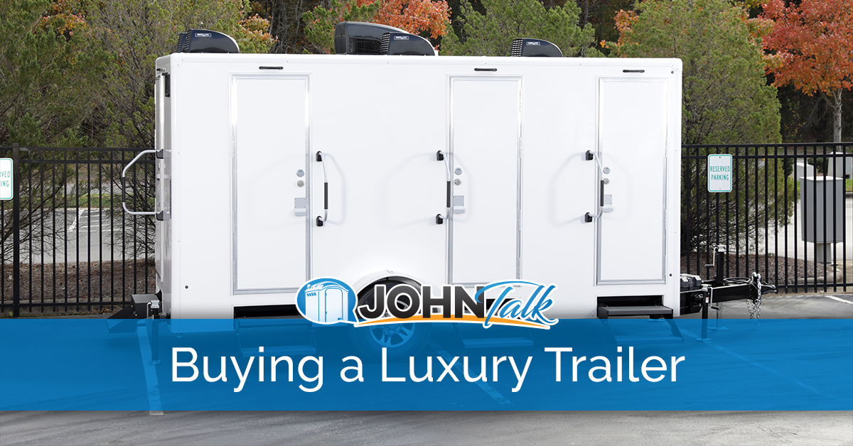 A white luxury restroom trailer in a parking lot with a fence and trees in the background