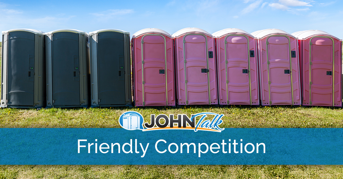 Gray portable toilets and pink portable toilets in a row in the grass