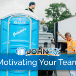 Two workers unloading a blue portable toilet from the back of a truck