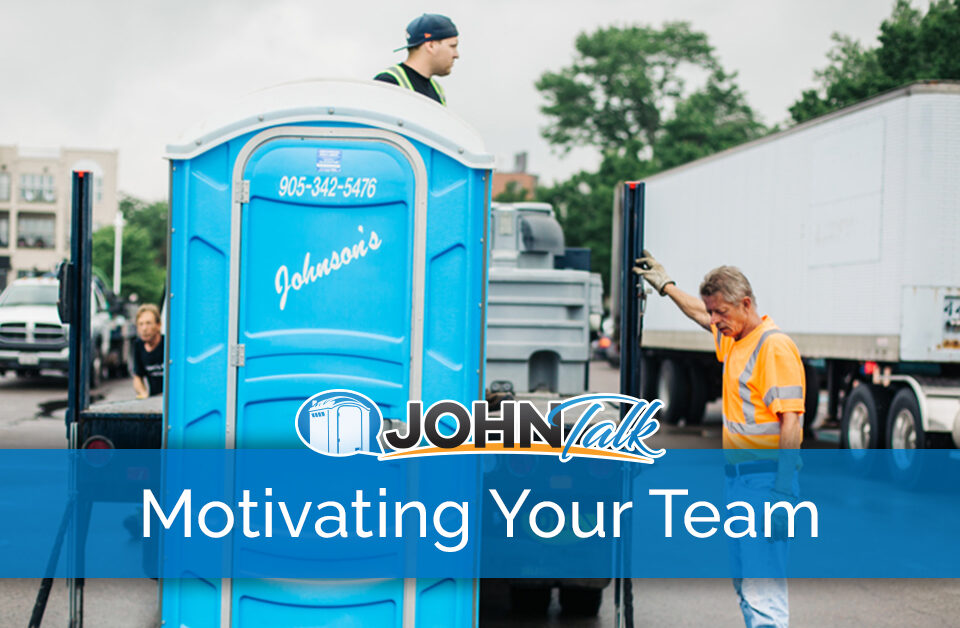 Two workers unloading a blue portable toilet from the back of a truck