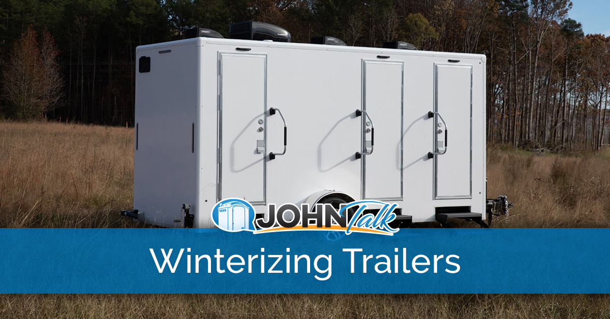 A white luxury restroom trailer in a grassy field with trees in the background